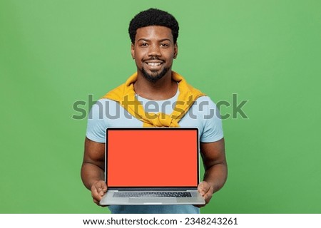 Young man of African American ethnicity 20s wear blue t-shirt hold use work on laptop pc computer with blank screen workspace area isolated on plain green background studio. People lifestyle concept