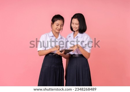 Two teenage Asian female students with short hair and long hair. wear school uniform Talking about homework, having a laptop and a pen for homework. Cute smile. Photo taken in pink background studio.