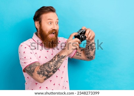 Portrait of impressed astonished man with cool tattoo wear flamingo t-shirt hold camera take photo isolated on blue color background