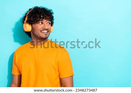 Photo of young guy listen wireless orange stylish headphones chill music lover look empty space isolated on aquamarine color background