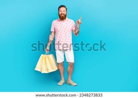 Full size photo of nice positive person hold boutique bags indicate finger empty space isolated on blue color background