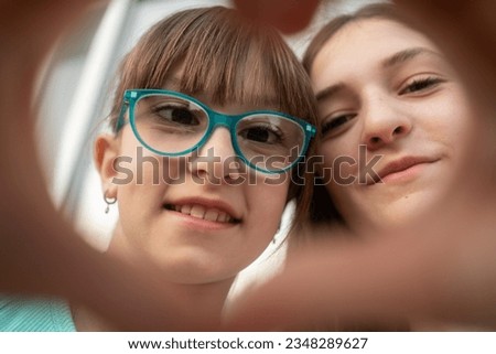 Self-portrait picture of smiling sisters make heart with hands pose look at camera together, happy  and girls children take selfie