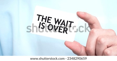 Man in blue sweatshirt holding a card with text THE WAIT IS OVER, business concept