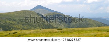 A high-angle view of a green and rocky mountain landscape with a prominent peak and a clear blue sky. Royalty-Free Stock Photo #2348295327