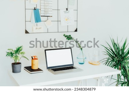 Modern Contemporary workplace - white desk with laptop mockup empty screen, grid mood board with pinned notes and plans, green plants, office supplies at work space in home office room interior