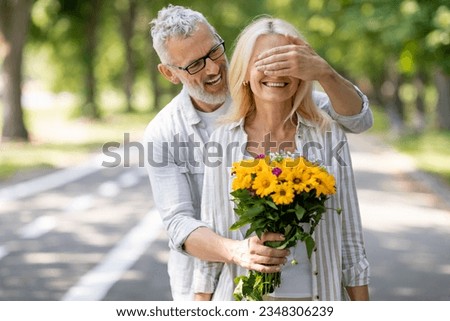 Loving Mature Husband Surprising Wife With Flowers, Covering Her Eyes And Giving Bouquet, Caring Man Greeting Spouse With Anniversary Or Making Romantic Surprise During Outdoor Date In Park