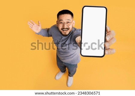 Great Promo. Excited Asian Man Showing Blank Smartphone With White Screen At Camera, Cheerful Guy Recommending New Mobile App Or Website, Standing Over Yellow Studio Background, Above Shot, Mockup Royalty-Free Stock Photo #2348306571
