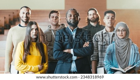 Portrait shot of African American male happy professor among mixed-races students in auditorium of University laughing n front of camera. Teacher and pupils concept. Posing for photo.