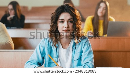 Close up of young pretty Caucasian female student sitting at desk in auditorium and reading textbook. College education concept. Girl read book at lection in University. Obtaining knowledge. Royalty-Free Stock Photo #2348319083