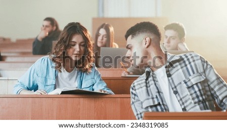 Caucasian beautiful girl reading textbook at lection and asking something guy with laptop. Whispering at seminar in college. University study concept. Female read book at class and talking. Students. Royalty-Free Stock Photo #2348319085