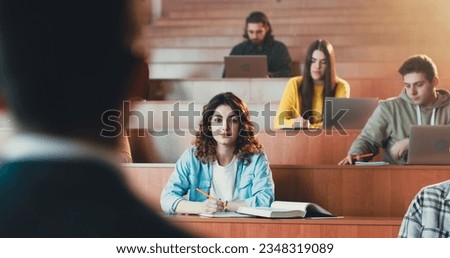 Young pretty Caucasian female student listening lection at college, writing down and using textbook. Reading book at seminar at high school. University study concept. Studying in classroom. Royalty-Free Stock Photo #2348319089
