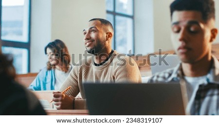 Handsome young African American male student sitting among others, listening to professor and noting information at lection. High school concept. Guy studying at University and writing down. Royalty-Free Stock Photo #2348319107