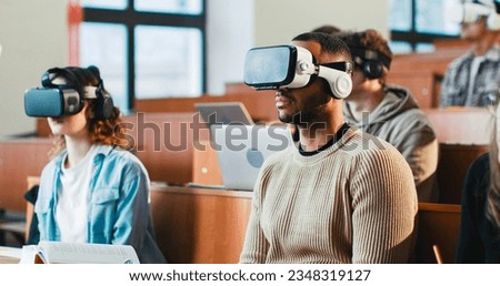 Back view of professor talking with laptop in front of mixed-races students in VR glasses. Multiethnic males and females learning high tech and listening to teacher at lection. Techonology education. Royalty-Free Stock Photo #2348319127