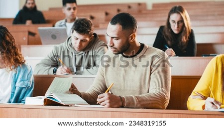 Young handsome African American male student listening lection at college, writing down and using textbook. Reading book at seminar at high school. University study concept. Guy studying Royalty-Free Stock Photo #2348319155