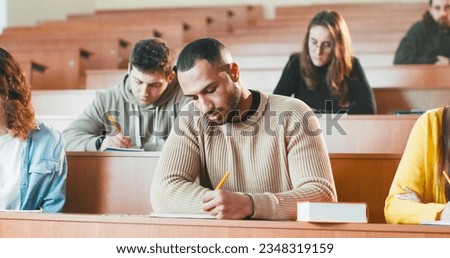 Young handsome African American male student listening lection at college, writing down and using textbook. Royalty-Free Stock Photo #2348319159