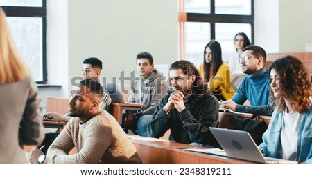 Back view on female professor at University lection talking and explaining material to multiethnic students in classroom. Woman teacher having speech. Guy student asking question. Rear. Royalty-Free Stock Photo #2348319211