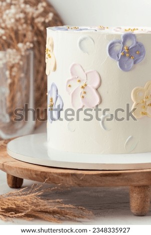 Birthday cake with white cream cheese frosting decorated with pastel butter cream flowers. Stylish cake for a girl on the wooden cake stand.