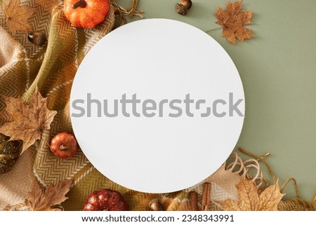 Get cozy with autumn decor. Top view photo of warm cashmere plaid, acorns, pumpkins, maple leaves on olive background with blank circle for promo or message