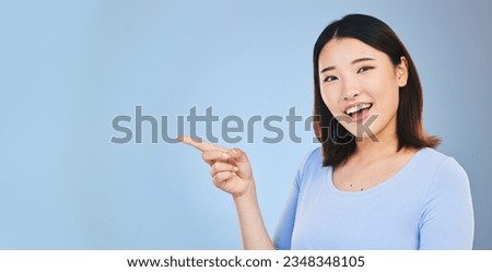 Asian woman, point and studio portrait with space, mockup and happy for promotion by blue background. Japanese student, girl and smile for review, opinion or feedback with choice, decision and sign