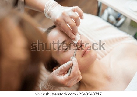 Skin care and cleaning in cosmetology clinic. Doctor cleaning pores on the client nose and face, using special cosmetology tools Royalty-Free Stock Photo #2348348717