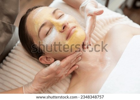 Young girl enjoying spa procedures with moisturizing, cleansing, brightening masks, while cosmetology specialist applying them to her face and neck. Skin care in modern beauty salon Royalty-Free Stock Photo #2348348757
