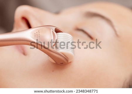 Using roller with micro needles for stimulation of skin regeneration and introduction of various rejuvenating drugs. Microneedle mesotherapy in cosmetology salon, close up of face of a girl client Royalty-Free Stock Photo #2348348771