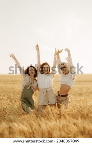 Excited young women in casual clothes raising arms and looking at camera while standing on dry grass meadow on sunny day and enjoying summer vacation in countryside Royalty-Free Stock Photo #2348367049