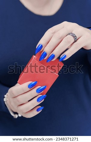 Female hands with blue long nails hold a gift box in red colors