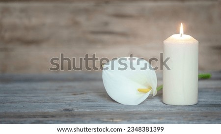 WHITE CALLA FLOWER NEXT TO A LIGHTED CANDLE ON WOODEN BACKGROUND. CONDOLENCE CARD. COPY SPACE. Royalty-Free Stock Photo #2348381399