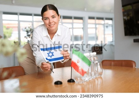 Woman secretary prepares an office for negotiations - she places flags of Iran and Israel the table