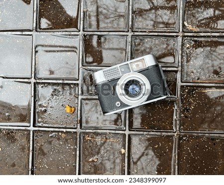 Old vintage camera with urban street style background and rain puddle texture reflections 
