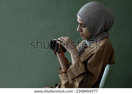 Pretty Muslim girl in hijab holding vintage camera over background in studio, check the neatness of the camera