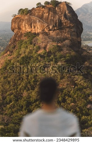 Man standing with back to camera looking at Lion Rock, Sigiriya Sri Lanka, wearing a baseball cap