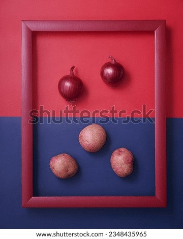 Red onions and potatoes shaped as smiling face in wooden picture frame on red and blue background