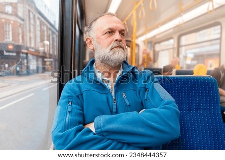 portrait of a bearded man in a blue jacket talking by phone on a bus or tram. Lifestyle concept