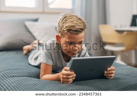 A cute young boy enjoys using tablet in bed.