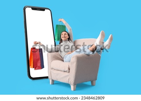 Happy woman with shopping bags sitting in armchair near big mobile phone on light blue background Royalty-Free Stock Photo #2348462809
