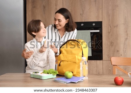 Mother helping her little son to pack schoolbag and lunch in kitchen Royalty-Free Stock Photo #2348463307