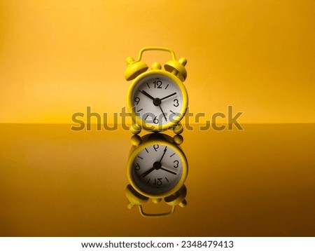 Yellow alarm clock on yellow background with reflection on a black acrylic board