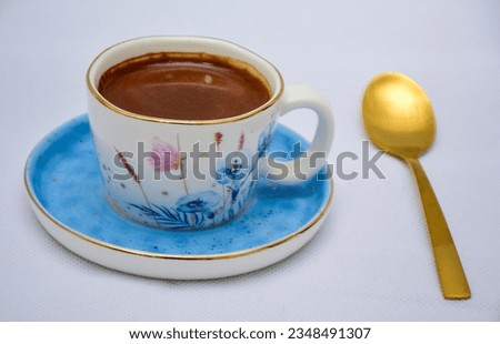 white and blue Cup of Turkish Coffee on a blue plate and gold plated tea spoon , flowers and butterfly on the ceramic mug 