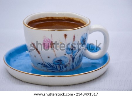white and blue Cup of Turkish Coffee on a blue plate and gold plated tea spoon , flowers and butterfly on the ceramic mug 