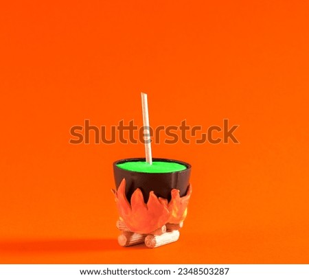 Small witch's pot with  potion is cooked on  fire on orange background. Halloween minimal poster.