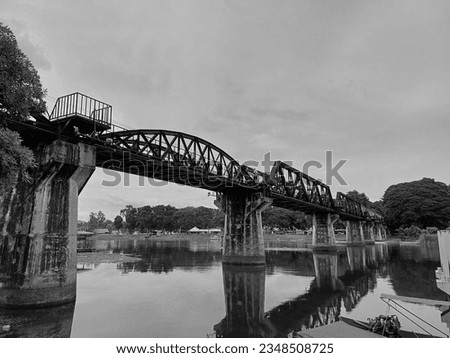 black and white photo ancient bridge spans a gentle river, embraced by vintage train tracks. The sky above is a canvas of fluffy clouds, completing this timeless picture.calm product antique bridge sp