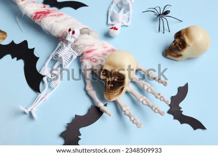 Skeleton hand with skulls and paper bats for Halloween celebration on blue background, closeup