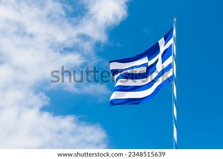 Flag of Greece against the blue sky with white clouds. Flag waving in the light wind in sunny summer day