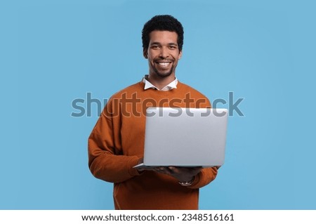 Happy man with laptop on light blue background