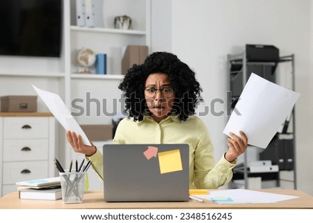 Deadline concept. Scared woman holding documents and looking at laptop in office