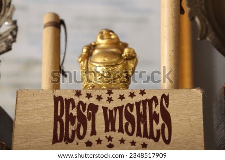 A golden Laughing Budha figurine with two pens standing on the side with Best Wishes written on the base of wood