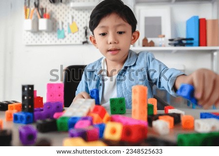 Asian Young Child Playing Colorful Plastic Cubes on Desk at Home. Learning and Education on Counting Cube in Math, Develop the Brain and Meditation while Playing. Royalty-Free Stock Photo #2348525633