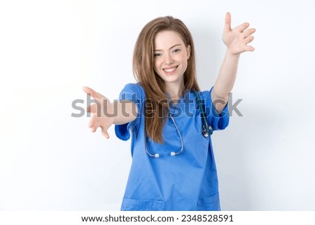 young beautiful doctor woman standing over white studio background looking at the camera smiling with open arms for hug. Cheerful expression embracing happiness. Royalty-Free Stock Photo #2348528591